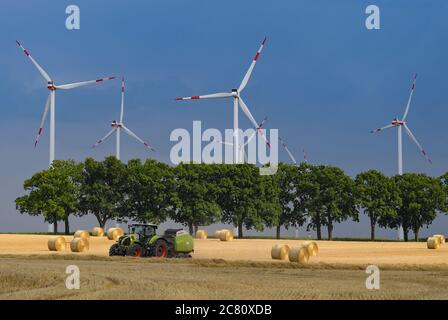 Petersdorf, Allemagne. 19 juillet 2020. Des nuages de tempête sombres passent au-dessus des éoliennes du parc éolien d'Odervorland dans le district d'Oder-Spree, tandis qu'au premier plan un agriculteur enfonce de la paille dans des rouleaux. Credit: Patrick Pleul/dpa-Zentralbild/ZB/dpa/Alay Live News Banque D'Images