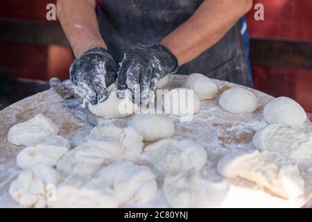 Gants noirs en chef coupe pâte crue en morceaux faire la pizza pain galettes. Processus de l'alimentation de rue. Bakary culinaire. Banque D'Images