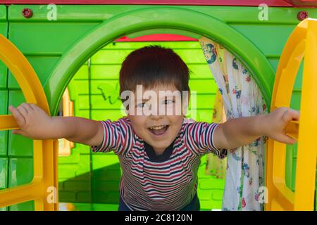 Un enfant de 3 ans dans un T-shirt rayé ouvre une fenêtre, joue dans une maison de jouets dans un centre pour enfants. Zone de jeux, développement des enfants Banque D'Images