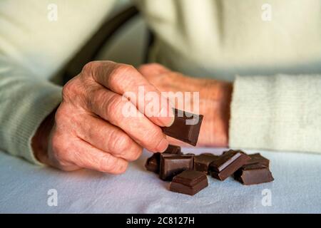 Senior dégustant des carrés de chocolat noir sur une surface douce à l'intérieur pendant un après-midi calme Banque D'Images