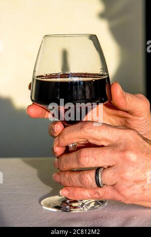 Les mains de la femme tiennent un verre à vin rempli de vin rouge riche sur un fond doux et léger Banque D'Images
