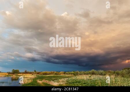 Ciel nuageux et sombre sur le terrain d'herbe sèche au bord de l'étang. Campagne rurale pluvieux nuages sinistre sur le champ sec d'herbe d'automne. Saleté Banque D'Images