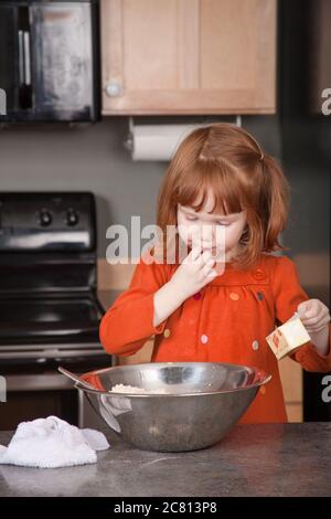 Une fillette de quatre ans se réglisse avec un doigt, savourant de la pâte à biscuits Banque D'Images
