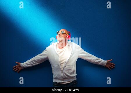 portrait d'un homme âgé écoutez de la musique avec des écouteurs et des lunettes de soleil jaunes illuminées par un rayon de lumière - homme âgé éclairé par un rayon de lumière lis Banque D'Images