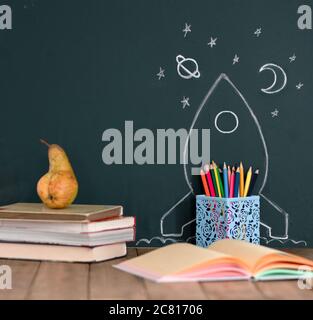 Concept de rentrée avec Rocket dessiné à la main et stars sur Blackboard. Crayons de couleur et livres sur une table en bois. Banque D'Images