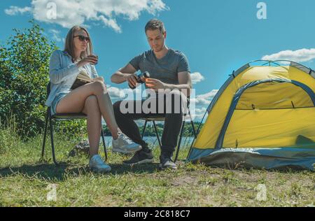 Femme et homme boivent du thé à partir de thermos près de la tente de camping au bord du lac. Banque D'Images