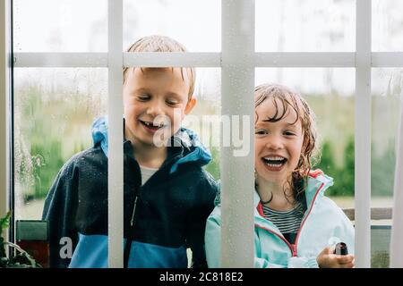 frère et sœur regardant à travers une fenêtre riant tout en jouant Banque D'Images