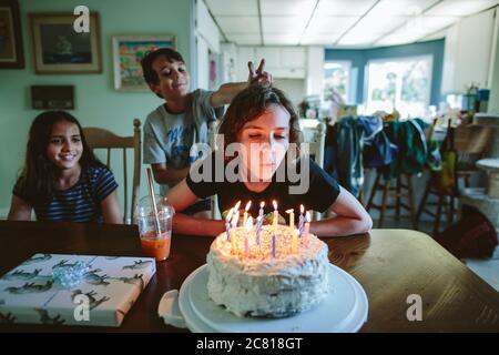 Une jeune fille souffle des bougies de son gâteau d'anniversaire avec frères et sœurs à proximité Banque D'Images