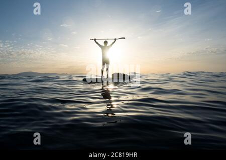 Concept: Victoire et bonheur. Homme sur un paddle surf. Au milieu de la mer bleue. Bras relevés maintenant l'oar. Regarder le lever du soleil. FLa Banque D'Images