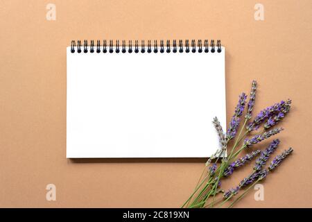 Bloc-notes vierge sur fond marron clair avec fleurs de lavande. Vue de dessus, plat, espace de copie Banque D'Images