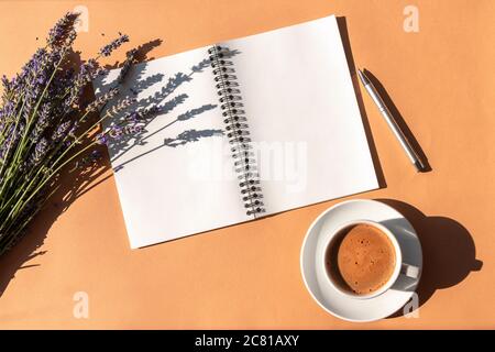Tasse à café et bloc-notes vierge sur fond beige avec fleurs de lavande et stylo. Vue de dessus, plat, espace de copie Banque D'Images