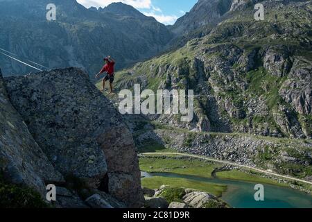 Lago Nero, Pinzolo, Italie - 2020 juillet 18: Jeune garçon à capuchon rouge et chapeau pratiquant la ligne de relâchement sur une corde suspendue entre deux sommets, grande hauteur a Banque D'Images