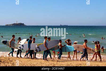 Groupe de jeunes hommes marchant le long de la plage à Somo portant des planches de surf prenant part à une leçon Santander Cantabria Espagne Banque D'Images
