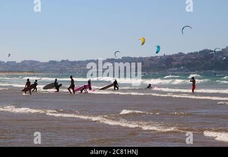 Paysage avec des surfeurs traînant leurs planches de surf entrant dans le surf avec des surfeurs cerf-volant dans la distance Santander Cantabria Espagne Banque D'Images