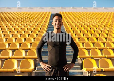 Le jeune sportif afro-américain se réjouattend avec plaisir à la caméra parmi les sièges vides du stade Banque D'Images