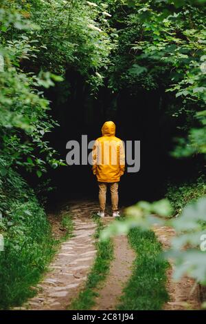 homme en couche de pluie jaune ponçant devant l'entrée sombre de la forêt Banque D'Images