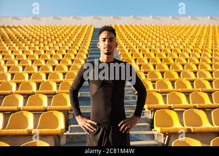 Un jeune sportif afro-américain regarde avec confiance les caméras parmi les sièges vides du stade Banque D'Images
