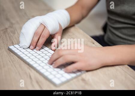 concept de soins de santé, de travail, de blessures et d'assurance - gros plan d'un homme avec bandage et gypse à portée de main en utilisant un ordinateur à la maison ou au bureau Banque D'Images