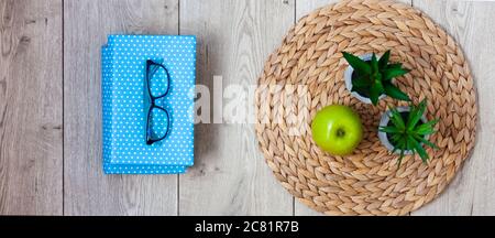 Retour à l'école, pile de livres en couvertures bleues, verres, pomme verte et plantes en pots sur un support en osier sur une table en bois. Enseignement à distance. Quar Banque D'Images