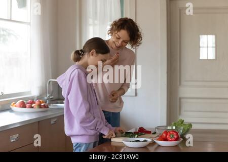 Une mère heureuse et une fille adolescente cuisent ensemble une salade à la maison Banque D'Images