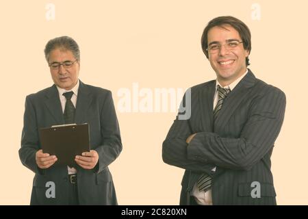 Les jeunes professionnels Persian businessman smiling with arms crossed et senior businessman reading perse sur presse-papiers Banque D'Images