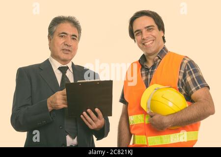 Persan senior businessman holding clipboard avec jeune homme persan construction worker smiling Banque D'Images