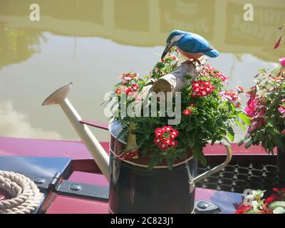 Un arrosoir décoré peut peint dans le style de l'art populaire de canal, rempli de plantation d'été et un oiseau modèle sur une bûche. Banque D'Images