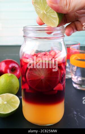 Image verticale de la main de l'homme presser la lime pour une bouteille de Sangria de vin rouge Banque D'Images