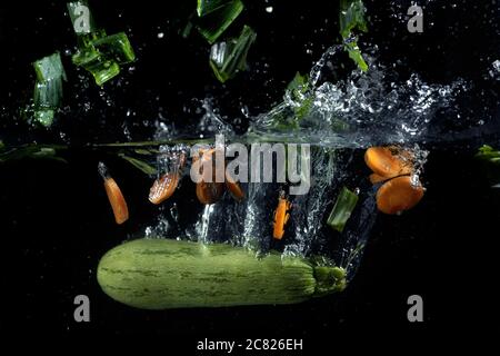 Légumes frais tombant dans l'eau avec des éclaboussures sur le noir arrière-plan Banque D'Images