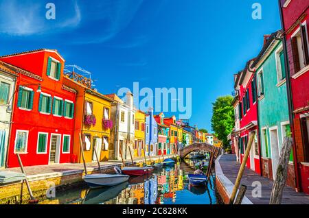 Maisons colorées de l'île de Burano. Bâtiments multicolores sur le remblai de fondamenta d'un canal étroit avec bateaux de pêche et pont en pierre, province de Venise, région de Vénétie, Italie. Carte postale Burano Banque D'Images