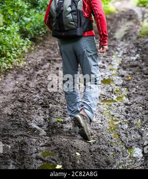 Vue arrière, partie basse d'un homme isolé marchant avec sac à dos sur un sentier boisé boueux dans la campagne britannique. Rambler de derrière dans la boue dans un cadre rural. Banque D'Images