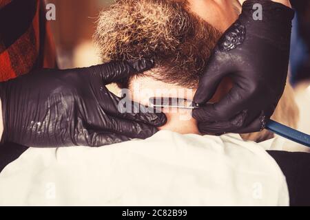 Vue rapprochée d'un jeune homme barbu qui obtient une coupe de barbe en coiffeur au salon de coiffure. Une forme parfaite. Banque D'Images