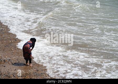 Une jeune fille asiatique, en train de pagayer dans la mer pendant une journée d'été au bord de la mer, entièrement vêtue. ROYAUME-UNI Banque D'Images