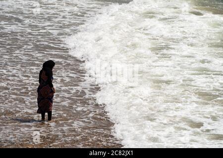 Une jeune fille asiatique, en train de pagayer dans la mer pendant une journée d'été au bord de la mer, entièrement vêtue. ROYAUME-UNI Banque D'Images