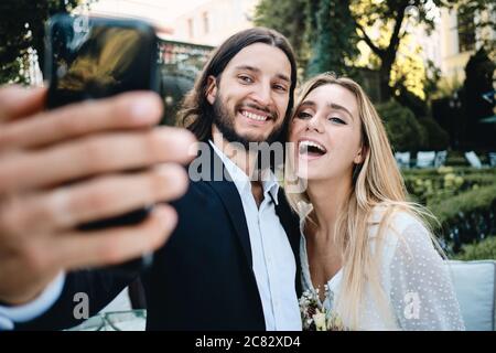 Jeune groom gai et mariée gai heureux de prendre le selfie dans le jardin du restaurant Banque D'Images