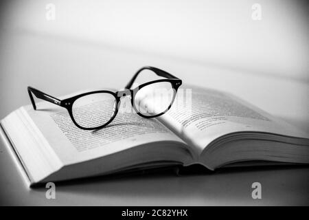 Prise de vue en niveaux de gris d'une paire de lunettes sur une ouverture livre sur fond blanc Banque D'Images