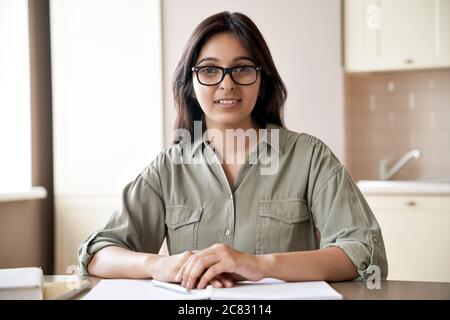 Jeune femme indienne souriante, enseignante, portant des lunettes, assise à table. Banque D'Images