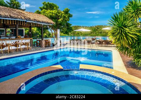 Belle piscine tropicale avec eau bleue et bar en plein air avec toit de chaume au bord de l'eau, par une journée ensoleillée. Banque D'Images