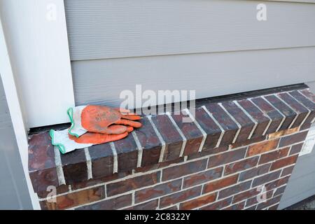 Paire de gants de travail orange pour jardin avec de la saleté sur une corniche de briques à l'extérieur; de la saleté incrustée sur les gants de cour utilisés pour le jardinage autour de la maison. Banque D'Images