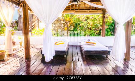 Une salle de massage en plein air, lumineuse et aérée, rustique, aux Philippines, avec deux lits simples sur un parquet et de jolis rideaux blancs de style boho. Banque D'Images