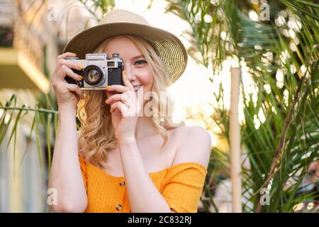 Portrait de jolie fille blonde dans le chapeau heureux de prendre la photo sur l'appareil photo rétro dans la rue Banque D'Images