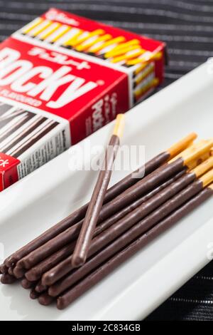 Image verticale des bâtonnets de chocolat Pocky placée sur une longue plaque blanche et un emballage en boîte. Banque D'Images