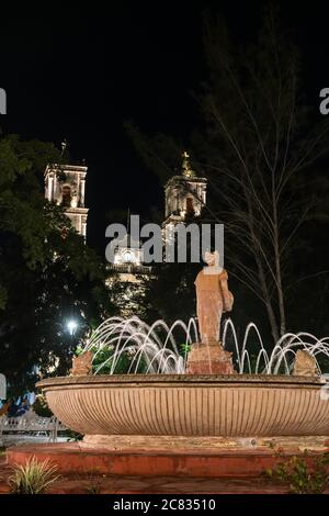 Une fontaine avec une statue d'une femme maya, éclairée la nuit, dans le parc Francisco Cantón Rosado. Derrière se trouve l'église de San Servasio. Valladolid, Yucatan, Banque D'Images