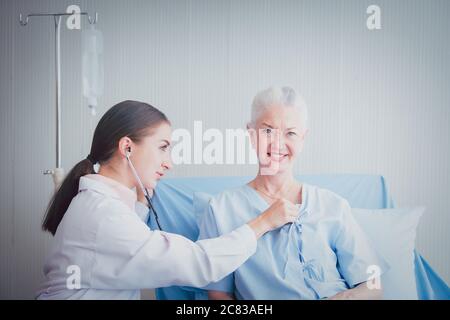 Une patiente âgée heureuse parle avec une femme médecin dans la chambre de l'hôpital. Médecin utiliser le poumon d'écoute du stéthoscope du patient âgé. Soins à domicile concep Banque D'Images
