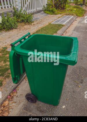 Ouvert grand vide poubelle en plastique vert vide en face de la maison moderne avec des arbres verts. Pas de déchets publics sur le côté de la route. Infectieux Banque D'Images