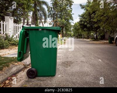 Ouvert grand vide poubelle en plastique vert vide en face de la maison moderne avec des arbres verts. Pas de déchets publics sur le côté de la route. Infectieux Banque D'Images