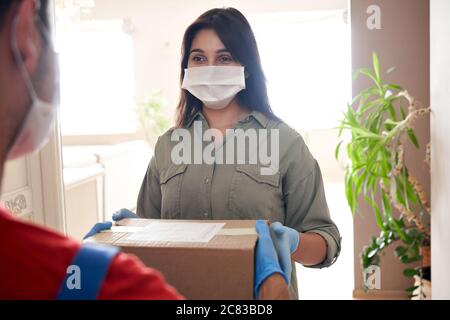 Une cliente indienne porte un masque facial tenant la boîte de livraison du courrier à la maison. Banque D'Images