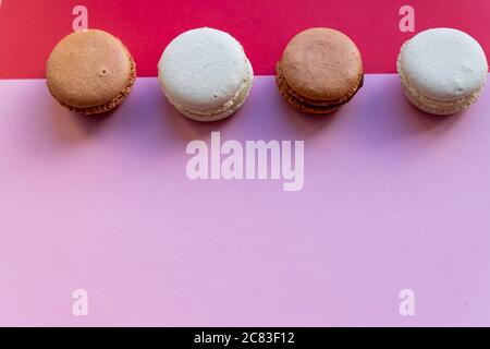 Macaron à gâteau coloré ou macaron, meringues blanches sur fond rouge et rose. Petits gâteaux aux amandes françaises sur la vue du dessus du dessert.biscuits sucrés français. Nourriture minimale Banque D'Images