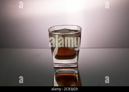 Verre de whisky avec morceaux de glace sur la table miroir. Image horizontale avec espace de copie. Banque D'Images