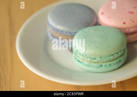 Vue de dessus sur les macarons français dans les tons pastel, plaque blanche sur une table en bois Banque D'Images